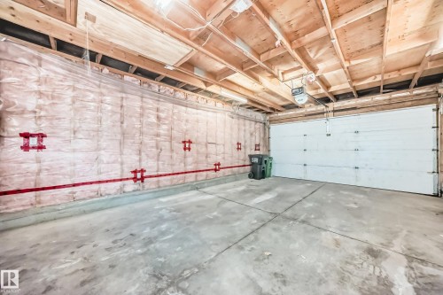 Unfinished garage space with concrete flooring, exposed wood beam ceiling, and a paneled garage door - 11727 83 Street Nw, Edmonton, AB - Indoor Photo Showing Garage