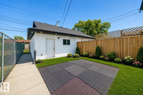 Virtually enhanced image of Paved patio area, manicured lawn, wood privacy fence with lattice accent, landscaped garden beds, and an exterior building with white siding - 11727 83 Street Nw, Edmonton, AB - Outdoor With Exterior