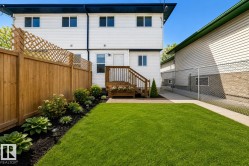 Virtually enhanced image of expansive green lawn with a landscaped garden bed, wood privacy fence, and a raised wood deck with stairs - 
