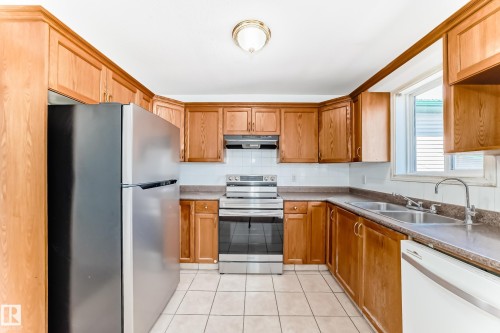 Kitchen with wood-finish cabinetry, tile flooring, stainless steel range, and double basin sink - 11727 83 Street Nw, Edmonton, AB - Indoor Photo Showing Kitchen With Double Sink