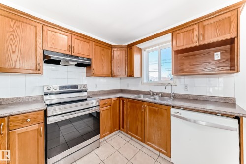 Kitchen with wood cabinetry, stainless steel range, double basin sink, and white tile backsplash - 11727 83 Street Nw, Edmonton, AB - Indoor Photo Showing Kitchen With Double Sink