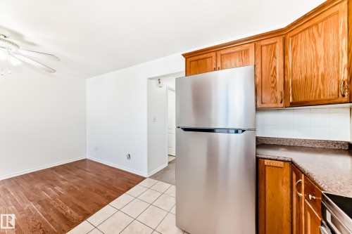 Kitchen and dining area featuring wood-finish flooring, light wood cabinetry, a stainless steel refrigerator, and a ceiling fan - 11727 83 Street Nw, Edmonton, AB - Indoor
