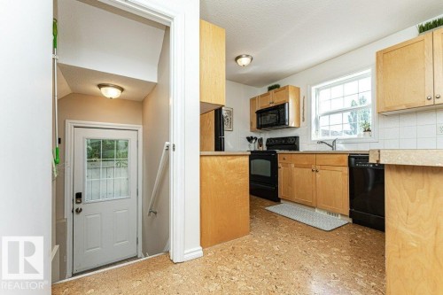 Kitchen with light wood-finish cabinetry, black appliances, a white tile backsplash, and cork-finish flooring - 1539 Kinross Road Nw, Edmonton, AB - Indoor Photo Showing Kitchen