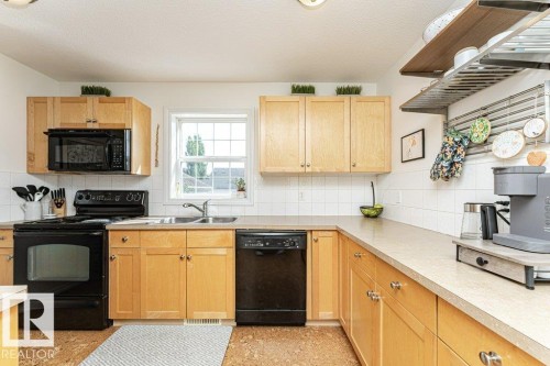 Light wood-finish cabinetry, black appliances, white tiled backsplash, and a double basin sink - 1539 Kinross Road Nw, Edmonton, AB - Indoor Photo Showing Kitchen With Double Sink