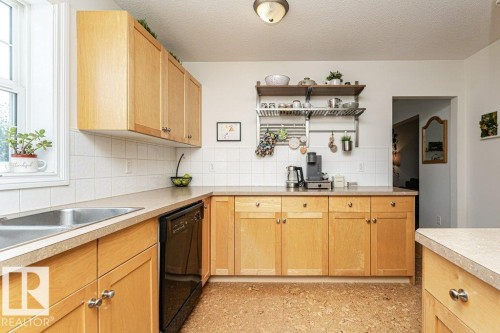 Light wood-finish cabinetry, solid surface countertops, a stainless steel double sink, white tile backsplash, and cork flooring - 1539 Kinross Road Nw, Edmonton, AB - Indoor Photo Showing Kitchen