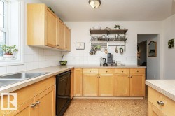 Light wood-finish cabinetry, solid surface countertops, a stainless steel double sink, white tile backsplash, and cork flooring - 