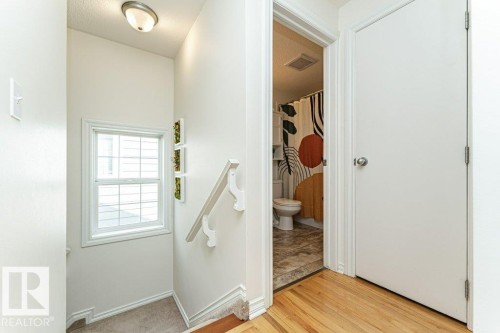 Hardwood flooring, white interior door, window with muntins, wall-mounted light fixture, white staircase railing - 1539 Kinross Road Nw, Edmonton, AB - Indoor Photo Showing Other Room