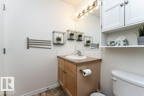 Bathroom featuring a wood-finish vanity with an integrated sink, a wall-mounted mirror, and overhead vanity lighting - 1539 Kinross Road Nw, Edmonton, AB - Indoor Photo Showing Bathroom