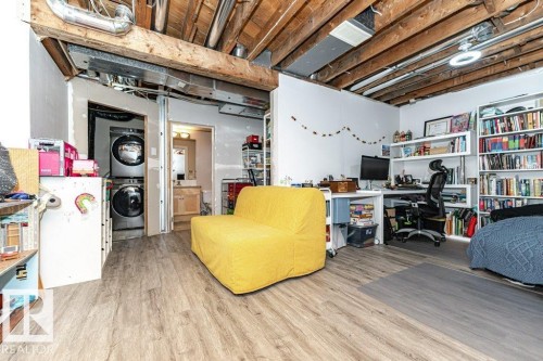 Exposed ceiling joists with visible ductwork, wood-finish flooring, integrated shelving, and a built-in stacked washer and dryer - 1539 Kinross Road Nw, Edmonton, AB - Indoor
