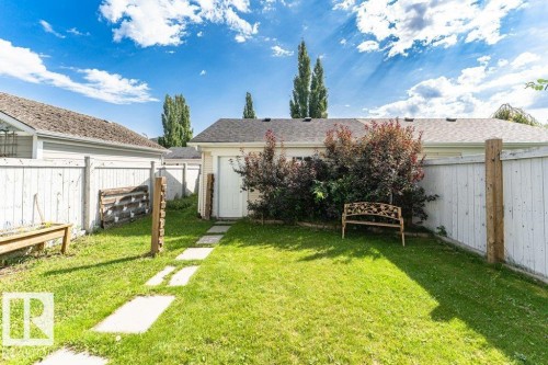 Expansive green yard featuring a concrete paver walkway, white privacy fencing, and a detached structure with an overhead door - 1539 Kinross Road Nw, Edmonton, AB - Outdoor