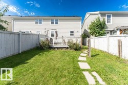 Expansive grassy yard area featuring a concrete paver pathway, wood fencing, and a raised wood deck - 
