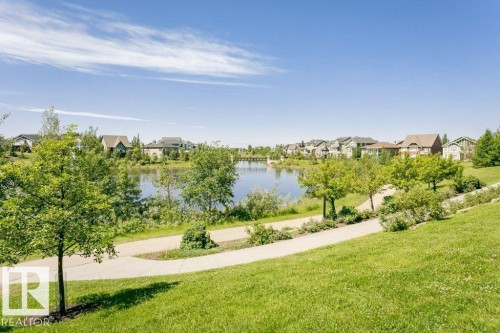 Expansive green space featuring a paved pathway, mature trees, and a tranquil lake - 1539 Kinross Road Nw, Edmonton, AB - Outdoor With View