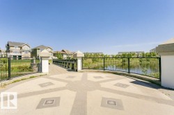 Paved outdoor area with decorative inlay, surrounded by a black metal fence and stone pillars - 