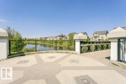 Paved patio with decorative inlay, black metal railing, and a wooden pedestrian bridge over a water feature - 