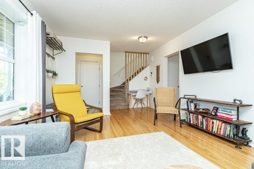 Hardwood flooring, white painted walls, natural light from a large window, built-in shelving, and a wood staircase with railing - 1539 Kinross Road Nw, Edmonton, AB - Indoor