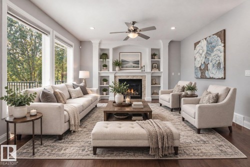 Spacious living area featuring wood-finish flooring, a built-in fireplace with a stone surround, and integrated shelving - 427 Windermere Road Nw, Edmonton, AB - Indoor Photo Showing Living Room With Fireplace