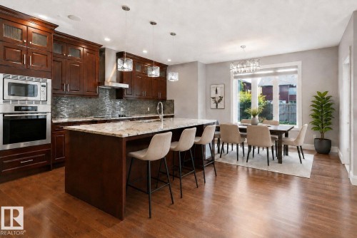 Gourmet kitchen with rich wood cabinetry, stainless steel appliances, a center island with a stone countertop, and wood-finish flooring - 427 Windermere Road Nw, Edmonton, AB - Indoor