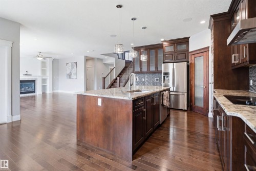 Hardwood flooring throughout, kitchen island with built-in sink, stainless steel appliances, dark wood-finish cabinetry, and a fireplace with built-in shelving - 427 Windermere Road Nw, Edmonton, AB - Indoor Photo Showing Kitchen With Upgraded Kitchen