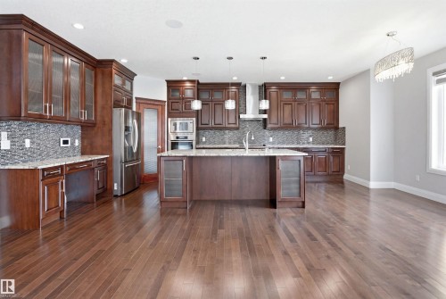 Spacious kitchen featuring rich wood cabinetry, stainless steel appliances, a large central island with seating, a mosaic tile backsplash, and light-toned countertops - 427 Windermere Road Nw, Edmonton, AB - Indoor Photo Showing Kitchen With Upgraded Kitchen