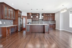 Spacious kitchen featuring rich wood cabinetry, stainless steel appliances, a large central island with seating, a mosaic tile backsplash, and light-toned countertops - 