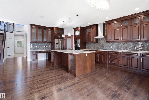 Wood-finish flooring throughout, kitchen island with built-in sink, stainless steel appliances, dark wood cabinetry, and mosaic tile backsplash - 427 Windermere Road Nw, Edmonton, AB - Indoor Photo Showing Kitchen With Upgraded Kitchen