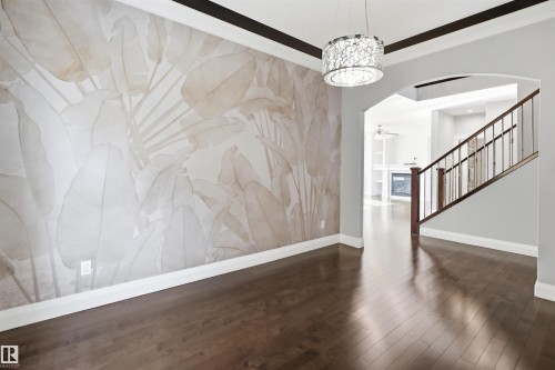 Hardwood flooring, decorative wall covering, architectural archway, metal spindle staircase, and a contemporary chandelier - 427 Windermere Road Nw, Edmonton, AB - Indoor