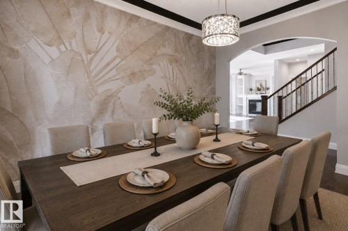 Dining area with accent wall, dark wood-finish flooring, a contemporary chandelier, an arched doorway, and a staircase with dark wood-finish railing - 427 Windermere Road Nw, Edmonton, AB - Indoor Photo Showing Dining Room