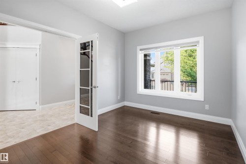 Dark wood-finish flooring, light grey painted walls, white trim, and a large window with a black metal railing - 427 Windermere Road Nw, Edmonton, AB - Indoor Photo Showing Other Room