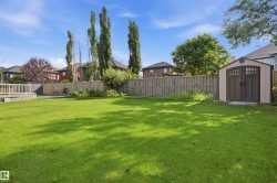 Expansive backyard featuring a manicured lawn, a raised wooden deck, a storage shed with double doors, and a wood privacy fence - 