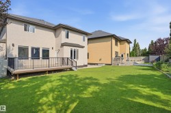 Expansive backyard featuring a manicured lawn, a raised deck with dark railings, and a privacy fence - 