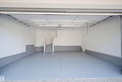 Expansive garage with painted concrete flooring, clean white walls, and a convenient interior access door - 