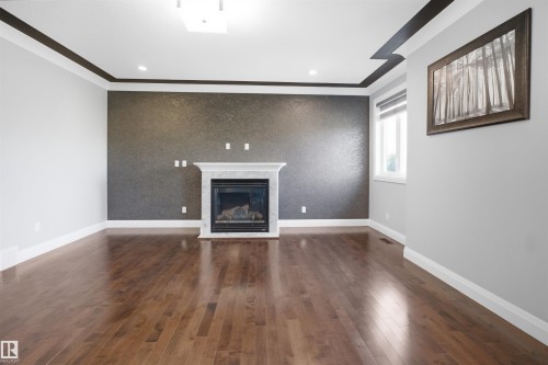 Hardwood flooring, fireplace with a marble-style surround, accent wall, crown molding, and a window with a roller shade - 427 Windermere Road Nw, Edmonton, AB - Indoor With Fireplace