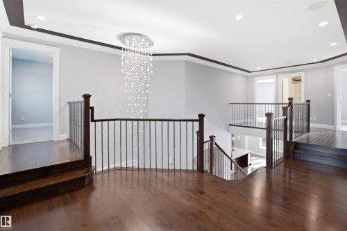 Hardwood flooring, dark wood railings with wrought iron spindles, recessed lighting, and a tiered crystal chandelier - 427 Windermere Road Nw, Edmonton, AB - Indoor Photo Showing Other Room