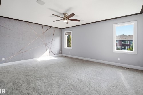 Spacious room with plush carpeting, two windows, a ceiling fan, and an accent wall featuring a geometric design - 427 Windermere Road Nw, Edmonton, AB - Indoor Photo Showing Other Room