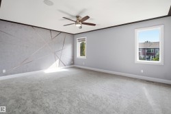 Spacious room with plush carpeting, two windows, a ceiling fan, and an accent wall featuring a geometric design - 
