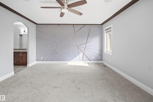 Textured accent wall with geometric detailing, light gray carpeting, ceiling fan with wood-finish blades, window with white trim, and a dark wood-finish vanity with a light countertop - 427 Windermere Road Nw, Edmonton, AB - Indoor Photo Showing Other Room