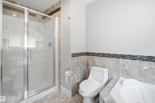 Glass-enclosed shower with a rainfall showerhead, tiled shower surround, integrated soaking tub, and floor-to-ceiling wall tiling - 427 Windermere Road Nw, Edmonton, AB - Indoor Photo Showing Bathroom