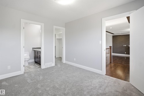 Carpeted room with light gray walls, an attached bathroom featuring a dark vanity with a light countertop, and an adjacent closet space - 427 Windermere Road Nw, Edmonton, AB - Indoor