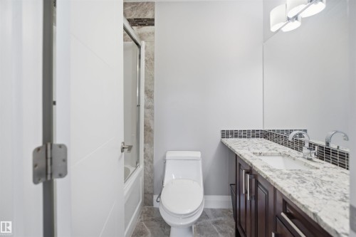 White flat panel door, full-size built-in bathtub with glass enclosure, white toilet, dark wood-finish vanity with drawer and cabinet storage, and a white countertop with an undermount sink - 427 Windermere Road Nw, Edmonton, AB - Indoor Photo Showing Bathroom