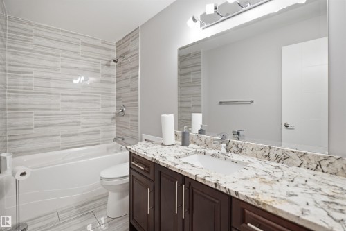 Bathtub with integrated shower, horizontal tile surround, vanity with stone countertop, undermount sink, and dark wood-finish cabinetry - 427 Windermere Road Nw, Edmonton, AB - Indoor Photo Showing Bathroom