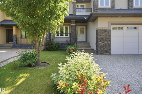 Front exterior featuring a stone accent façade, exposed aggregate driveway, attached garage with transom windows, and mature landscaping with a deciduous tree - 427 Windermere Road Nw, Edmonton, AB - Outdoor With Balcony With Facade