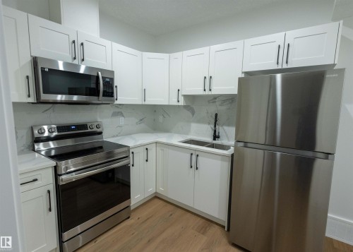 Contemporary kitchen featuring white cabinetry, stainless steel appliances, marble-look backsplash, and wood-finish flooring - 9632 #1 And #2 110 Ave Nw, Edmonton, AB - Indoor Photo Showing Kitchen With Double Sink