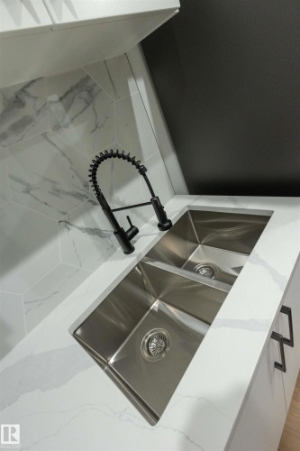 Dual stainless steel sinks with a matte black pull-down faucet, set into a white countertop with subtle veining - 9632 #1 And #2 110 Ave Nw, Edmonton, AB - 