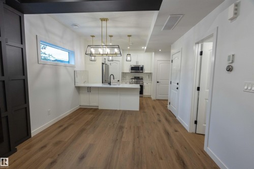 Wood-finish flooring, white cabinetry, stainless steel appliances, modern lighting fixtures, and a white countertop with a matte black faucet - 9632 #1 And #2 110 Ave Nw, Edmonton, AB - Indoor Photo Showing Kitchen With Upgraded Kitchen