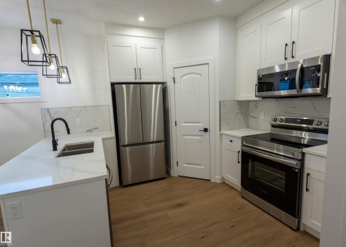 White shaker cabinetry, stainless steel appliances, wood-finish flooring, white countertop, and marble-look backsplash - 9632 #1 And #2 110 Ave Nw, Edmonton, AB - Indoor Photo Showing Kitchen With Double Sink With Upgraded Kitchen