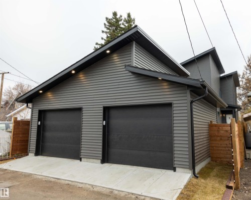 Dual black garage doors with exterior lighting, gray horizontal siding, black gutters, and a wood privacy fence - 9632 #1 And #2 110 Ave Nw, Edmonton, AB - Outdoor With Exterior