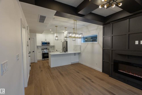 Wood-finish flooring throughout, kitchen with white cabinetry and stainless steel appliances, built-in electric fireplace, recessed lighting, and a coffered ceiling - 9632 #1 And #2 110 Ave Nw, Edmonton, AB - Indoor