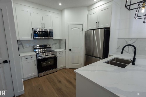 Kitchen featuring white shaker cabinetry, stainless steel appliances, light-toned countertops, a black gooseneck faucet, and wood-finish flooring - 9632 #1 And #2 110 Ave Nw, Edmonton, AB - Indoor Photo Showing Kitchen With Double Sink