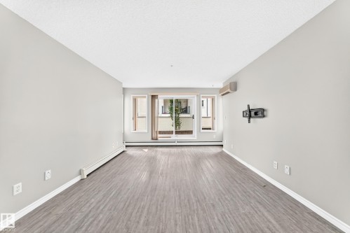 Light gray interior paint with wood-finish flooring, white trim, and a wall-mounted air conditioning unit - #137 9704 174 St Nw, Edmonton, AB - Indoor Photo Showing Other Room