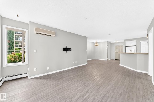 Spacious open-concept living area with wood-finish flooring, a contemporary ceiling fixture, and ample natural light from a large window - #137 9704 174 St Nw, Edmonton, AB - Indoor Photo Showing Other Room